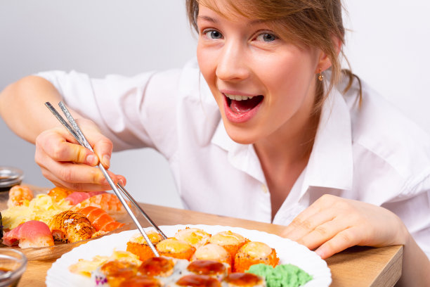 饥饿的女孩和日本食物。胃口大开的女孩高兴地吃着寿司。金发女郎用筷子吃饭。放大的照片。图片下载