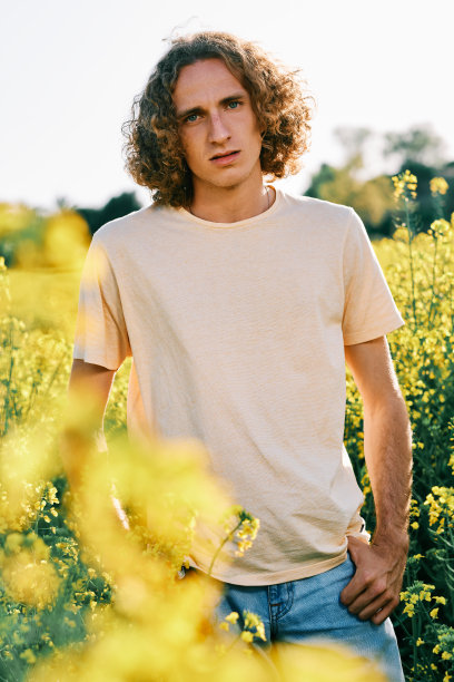 在一个阳光明媚的春日里，一个卷发的年轻人在油菜地里看着照相机图片下载