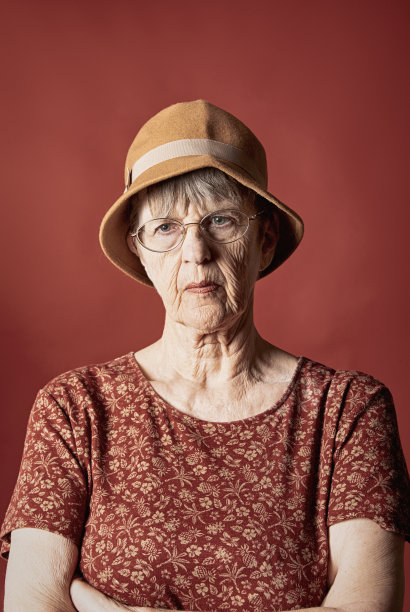 70多岁的老妇人双臂交叉，看起来很严肃，红色背景上有复印空间图片下载