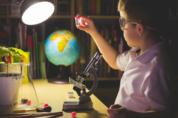 在一间暗室的桌子旁，一个男孩用显微镜进行科学实验。一位年轻的科学家正在家庭实验室里做实验。儿童早期发育。调色和人工噪音图片下载
