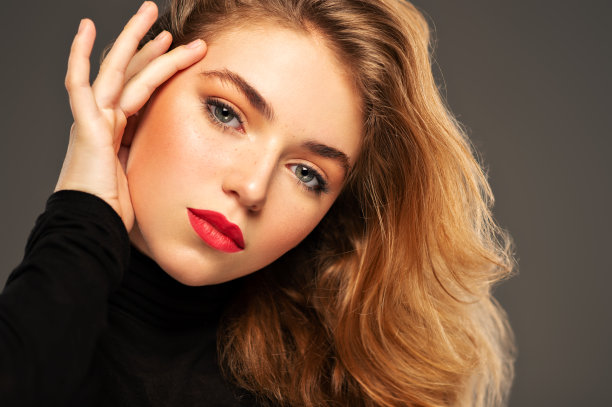 一个年轻的成年女孩的特写肖像长卷发。一名时装模特在工作室摆姿势的照片。漂亮的年轻女人，红唇看着镜头。美丽的肖像。图片下载