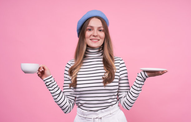 一个可爱的女士在时尚贝雷帽与一杯咖啡和茶托的肖像。图片下载