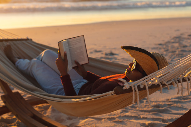 混血女人在海滩度假躺在吊床上看书在日落图片下载