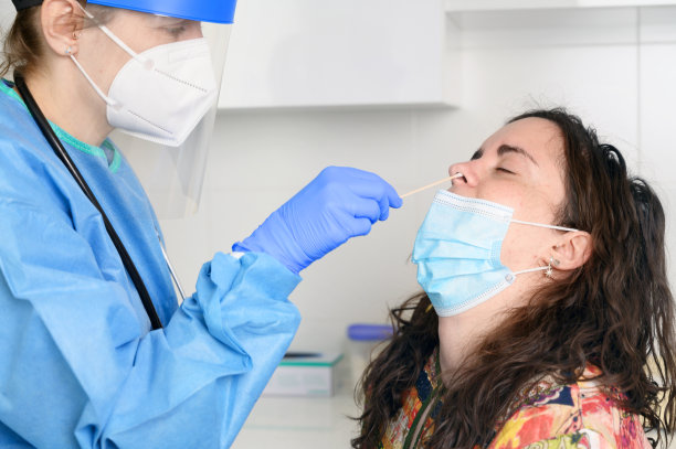 穿防护服的护士从一名年轻女性病人身上取鼻拭子样本。COVID-19概念。高质量的照片图片下载
