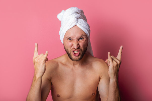 一名头上裹着毛巾、蓄着胡须的年轻人在粉色背景上做了一只山羊的手势图片下载