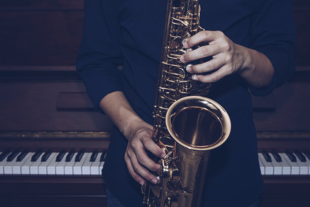 靠近萨克斯手演奏低音萨克斯乐器的钢琴背景图片下载