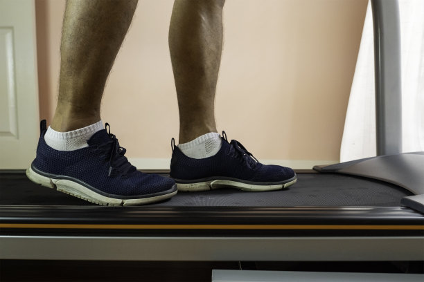 一个男人穿着蓝色运动在一个私人房间的跑步机上行走的特写。运动的概念，健身和健康的生活方式。图片下载