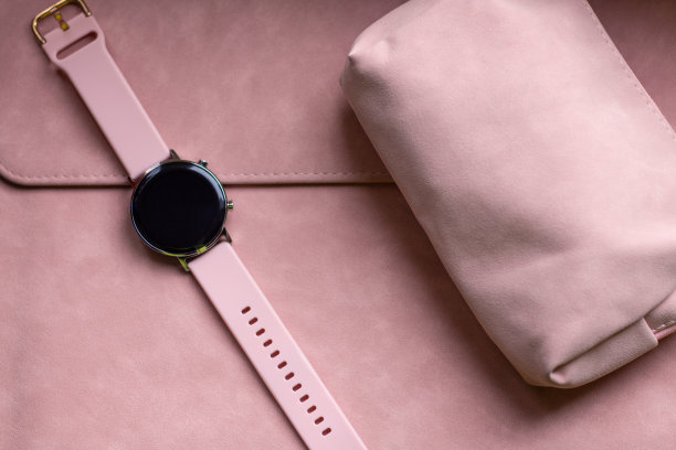 为女孩们设计的软粉色现代小工具。粉红色的笔记本电脑盒上放着一只带粉色表带的智能手表素材图片