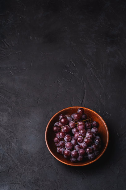 新鲜成熟的葡萄浆果在棕色的木碗上，黑色的石头背景，角度查看拷贝空间图片下载