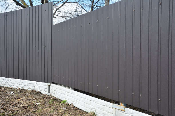 这是一个由金属波纹灰色栅栏板组成的住宅围墙的特写，安装在一个正在转动、改变方向的砖基础上。图片下载