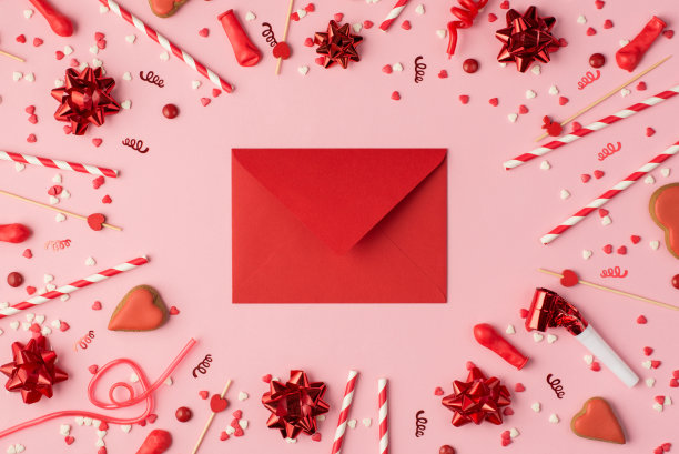 顶视图照片的生日组成与红色的缎带星星，蛇形的五彩纸屑心形饼干，明亮的装饰和红色封闭的信封在中间的柔和的粉红色背景与copyspace图片下载