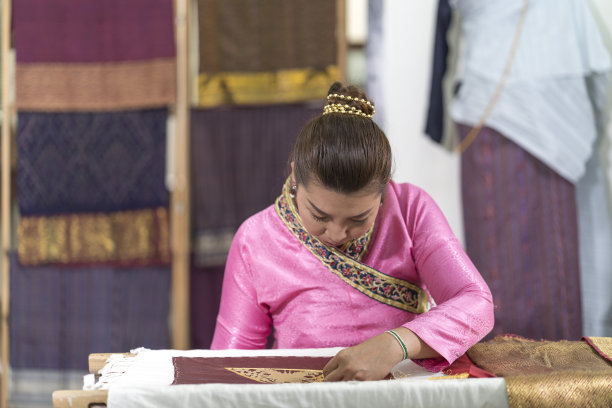 工艺品和工艺。年轻女子在缝丝绸。亚洲妇女在丝绸上绣金线。图片下载