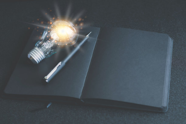 灯泡和黑色空白笔记本或普通记事本或日记本或日记，用于书写文字和信息与笔在桌子上或书桌作为背景与复制空间。仍然生活方式照片的概念。图片下载