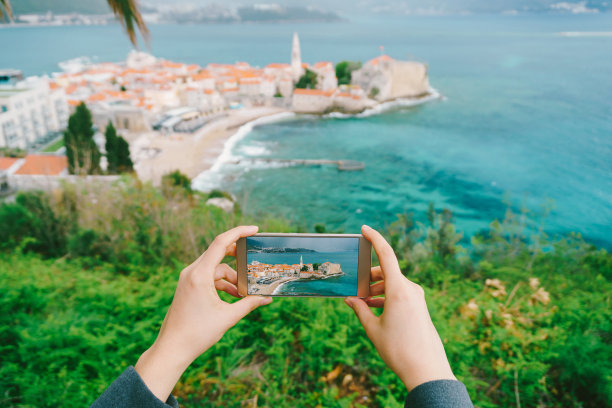 手拿着智能手机的照片。远处是一个古老的小镇。黑山共和国图片下载