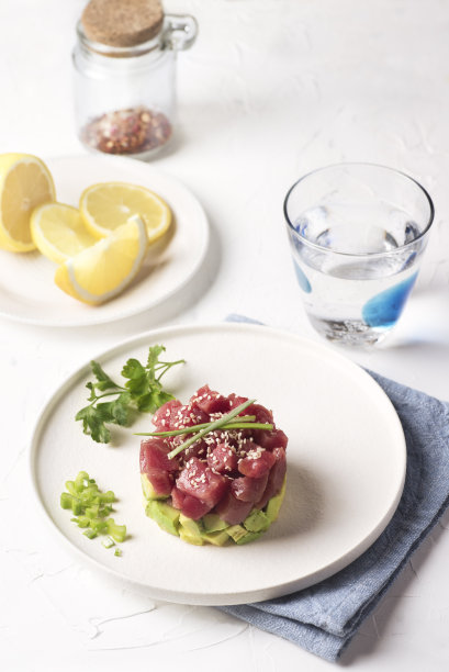 夏日塔塔金枪鱼塔塔配鳄梨、香料、芝麻、新鲜绿洋葱和柠檬，配以一道简约的白色菜肴。夏季鱼菜单，特写图片下载