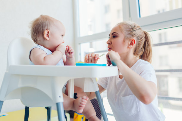 母亲节。妈妈在家用水果喂小婴儿。家人一起吃饭。婴儿坐在儿童座椅上图片下载
