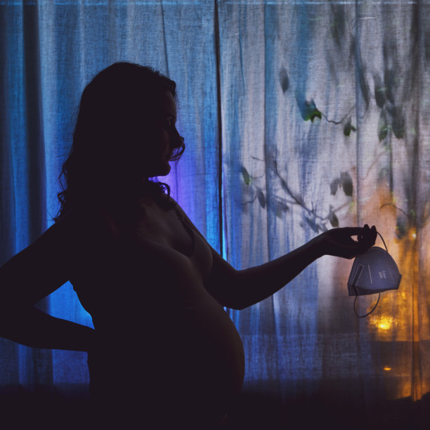 一个孕妇的夜晚剪影在窗边，她的手拿着一个摘掉的医用口罩ffp2图片下载