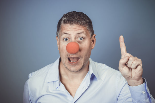 中年男子蓝色衬衫和红色小丑鼻子在蓝色背景下摆姿势图片下载