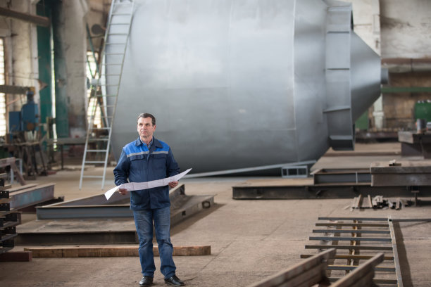 冶金工厂。工厂的工人有一个时间表。一位老人站在一家大企业的后面。工厂的员工图片下载