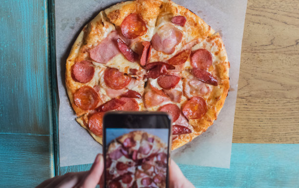 一个博主女孩坐在咖啡馆里用智能手机拍披萨。在社交网络、视频博客和照片博客中工作。创建互联网内容和食物摄影的概念。图片下载