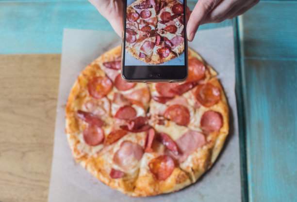 一个博主女孩坐在咖啡馆里用智能手机拍披萨。在社交网络、视频博客和照片博客中工作。创建互联网内容和食物摄影的概念。图片下载