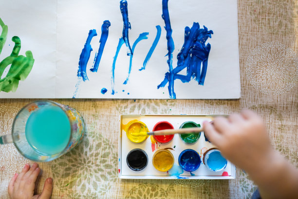 俯视图的小孩子正在画与明亮的油漆在纸上，近。图片下载