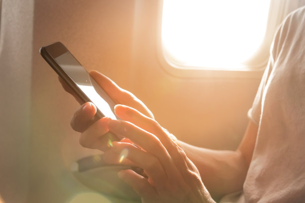 一个女人的手拿着一个黑色的智能手机和空白的桌面屏幕在机舱旁边的窗口飞机图片下载