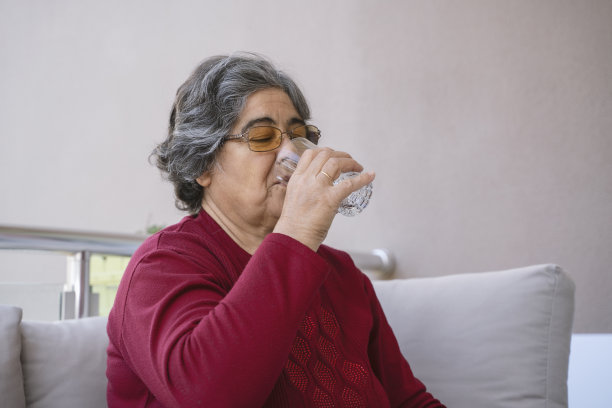 老妇人坐着感觉不舒服，手里拿着药加了一杯水图片下载