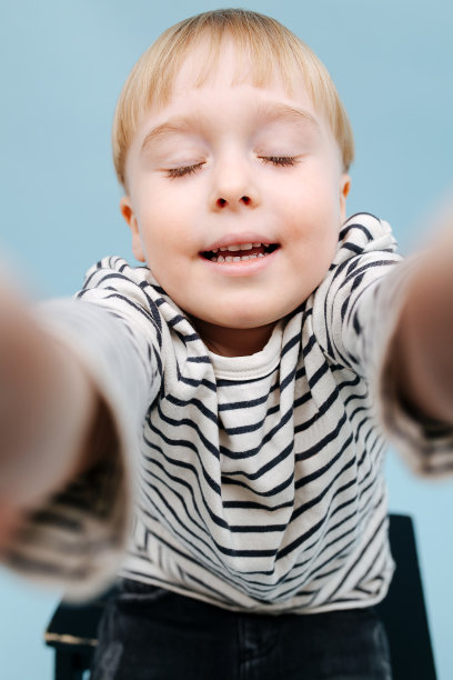 有趣的金发男孩坐在踏凳上。在蓝色背景图片下载
