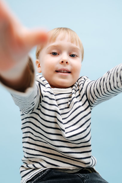 金发小男孩伸手去拿相机。在蓝色背景图片下载