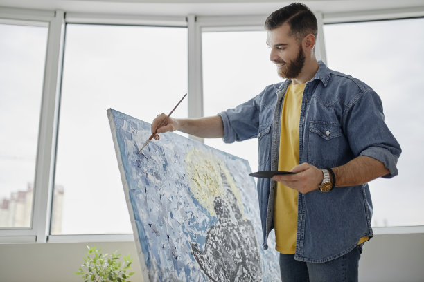 肖像有才华的胡子艺术家绘画画架上的画和微笑而享受工作在宽敞的艺术工作室图片下载