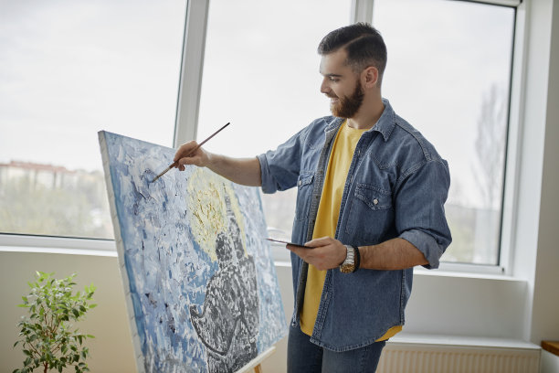 肖像有才华的胡子艺术家绘画画架上的画和微笑而享受工作在宽敞的艺术工作室图片下载