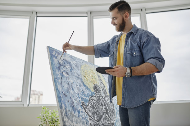 肖像有才华的胡子艺术家绘画画架上的画和微笑而享受工作在宽敞的艺术工作室图片下载