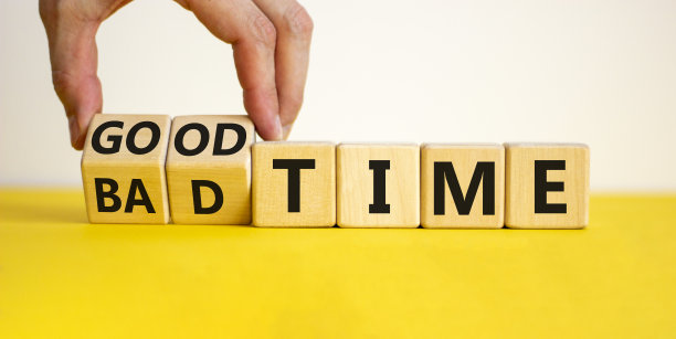 好或坏的时间符号。商人把木制立方体变成了“坏的时间”，把单词“好时间”。漂亮的黄色表，白色背景，拷贝空间。商业和好或坏的时间概念。图片下载