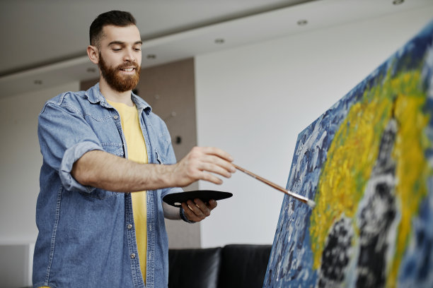 肖像有才华的胡子艺术家绘画画架上的画和微笑而享受工作在宽敞的艺术工作室图片下载