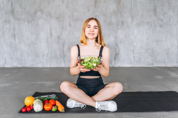 一个穿着运动服的运动女人正坐在地板上吃着健康的食物。图片下载