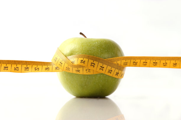 苹果和卷尺在灯光背景上的特写图片下载