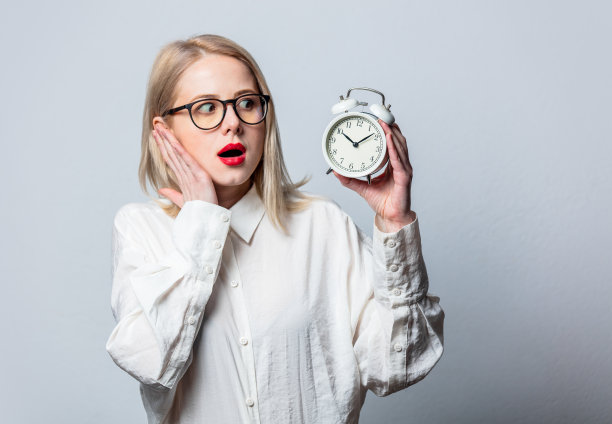 美丽的金发在白色衬衫与闹钟在白色的背景肖像图片下载