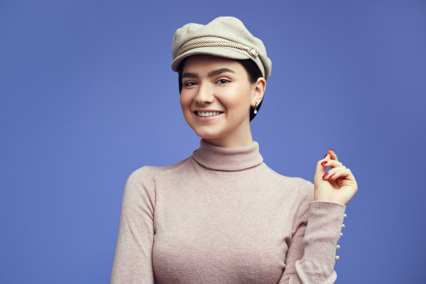 肖像的快乐美丽的女人，穿着毛衣和帽子，微笑而摆姿势在工作室在紫色的背景图片下载