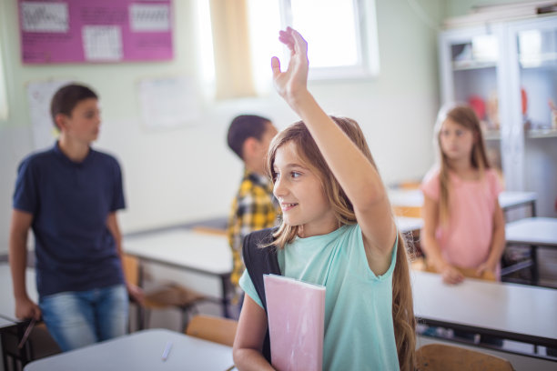 微笑的女学生拿着书包看着相机。焦点放在前景。图片下载