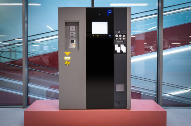 现代化的灰黑色停车售票机，在玻璃墙前面的停车场和自动扶梯的背景。灯在玻璃上反射。图片下载