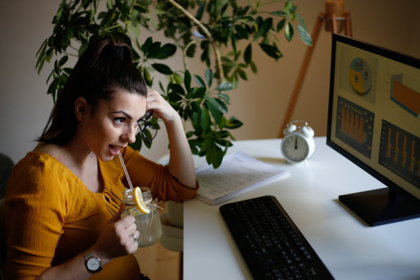 年轻的商务女孩看着桌上放着柠檬水和杯子的笔记本电脑。库存图片图片下载