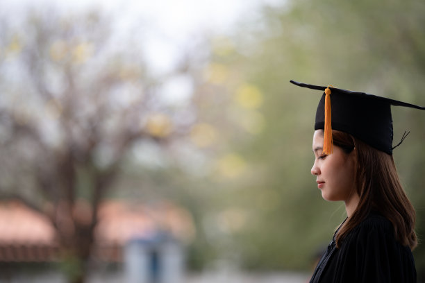 一位年轻快乐的亚洲女子大学毕业生穿着毕业礼服和学位帽持有学位证书庆祝教育成就在大学校园。教育库存图片图片下载