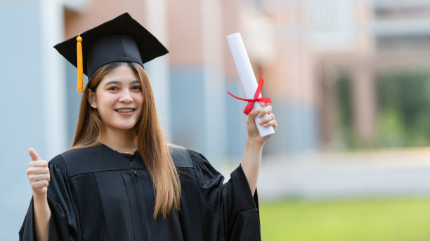 一位年轻快乐的亚洲女子大学毕业生穿着毕业礼服和学位帽持有学位证书庆祝教育成就在大学校园。教育库存图片图片下载