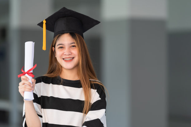 一名年轻的亚洲女子大学毕业生穿着毕业礼服和学位帽持有学位证书庆祝教育成就在大学校园。教育库存图片图片下载