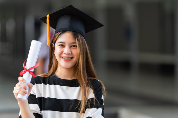 一名年轻的亚洲女子大学毕业生穿着毕业礼服和学位帽持有学位证书庆祝教育成就在大学校园。教育库存图片图片下载