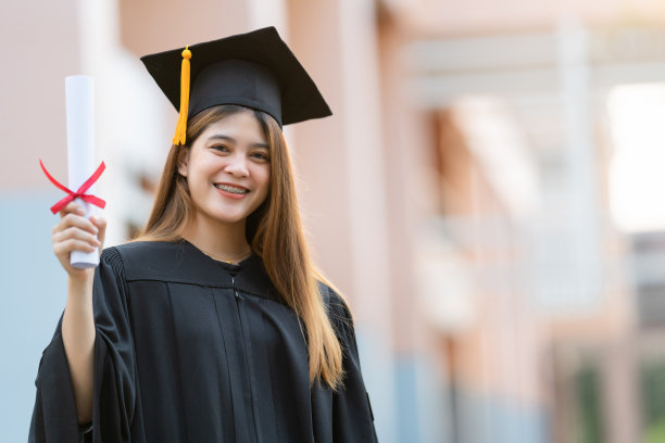 一位年轻快乐的亚洲女子大学毕业生穿着毕业礼服和学位帽持有学位证书庆祝教育成就在大学校园。教育库存图片图片下载