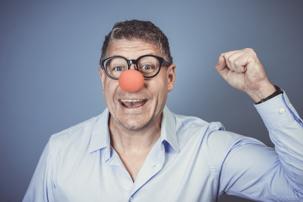 蓝色衬衫，黑色眼镜，红色小丑鼻子的商人在蓝色背景前摆姿势图片下载