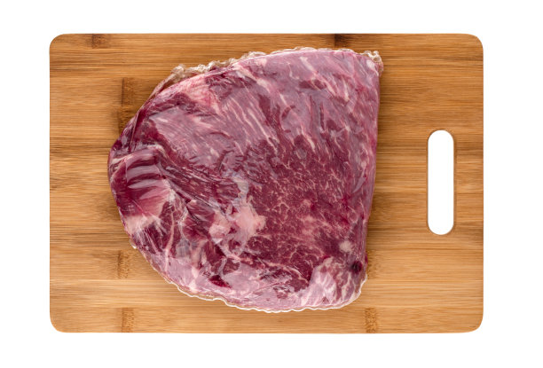 真空包装的肉在白色的背景。真空袋里的牛肉在一个板上特写。图片下载