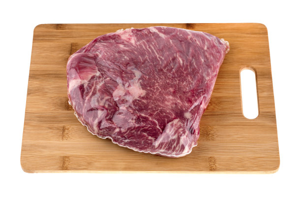 真空包装的肉在白色的背景。真空袋里的牛肉在一个板上特写。图片下载